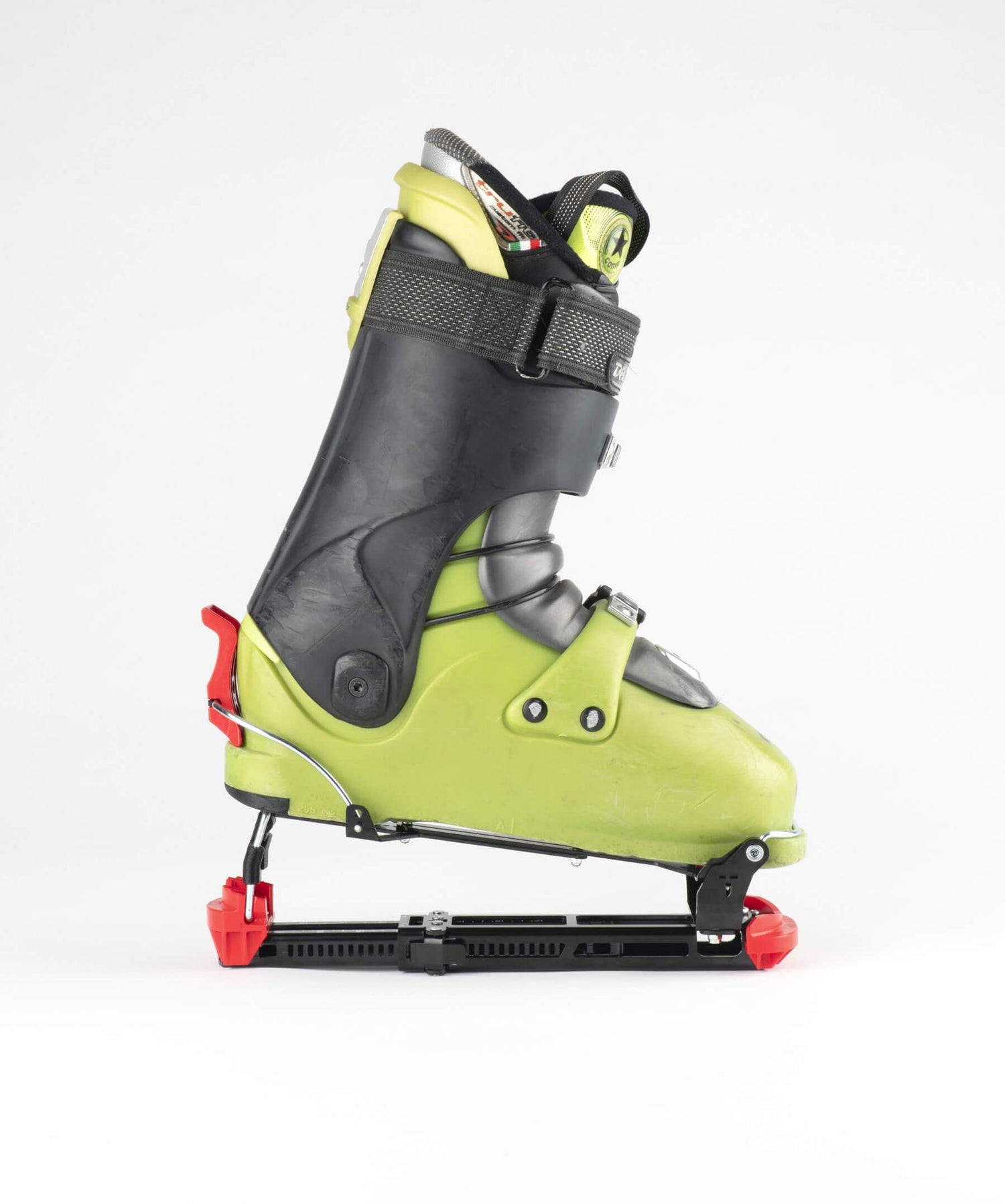 A single ski boot with an attached sled base, featuring a lime green shell, black protective armor, gray buckles, and red release levers, photographed against a seamless white background.